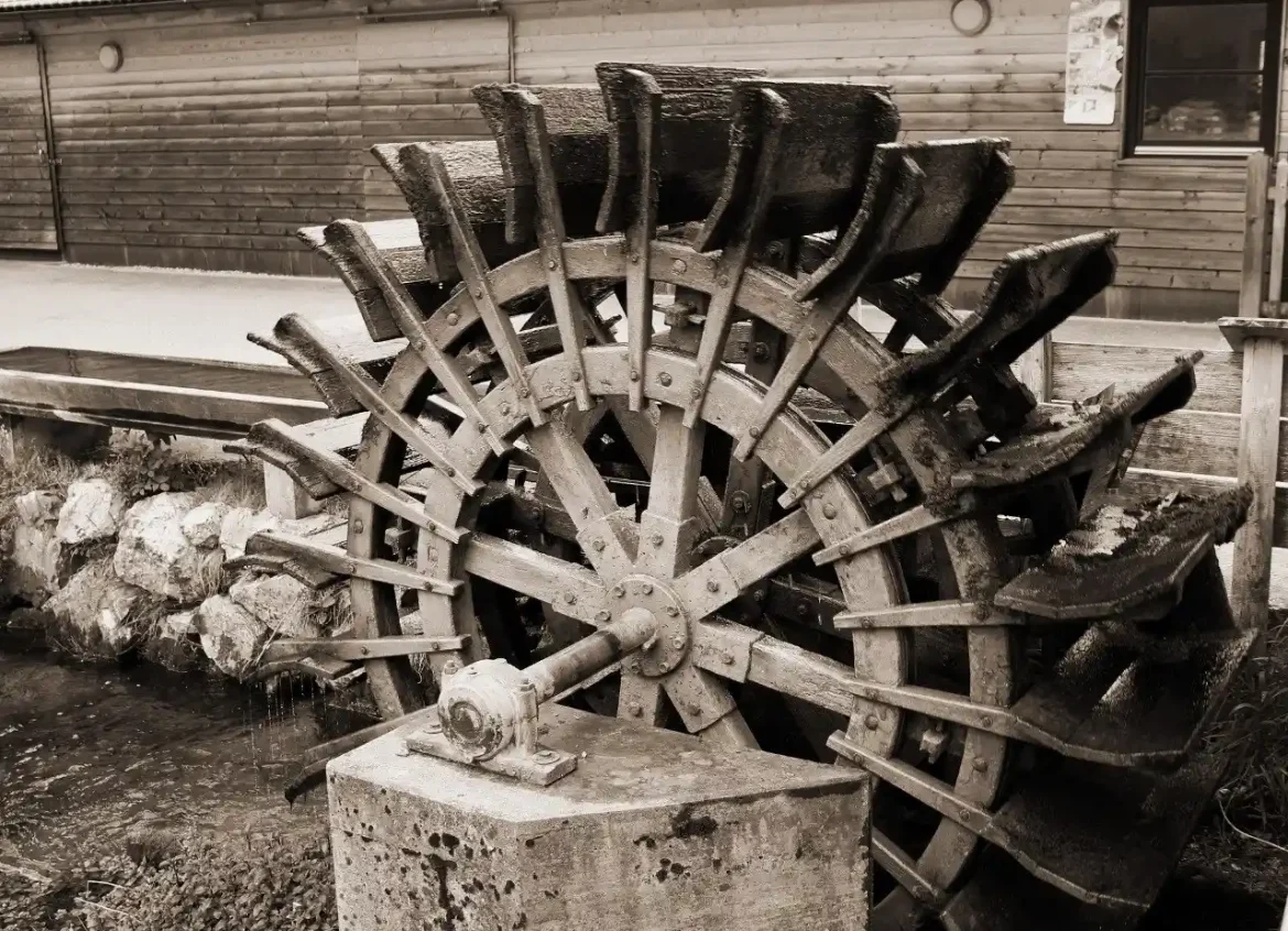 Rueda hidráulica de madera de un molino histórico instalada junto a un canal de agua y una estructura de piedra y madera